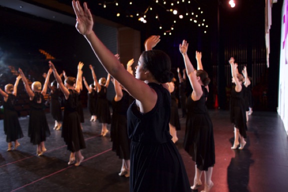 Arms raised high, dancers on stage move through their choreographed routine.